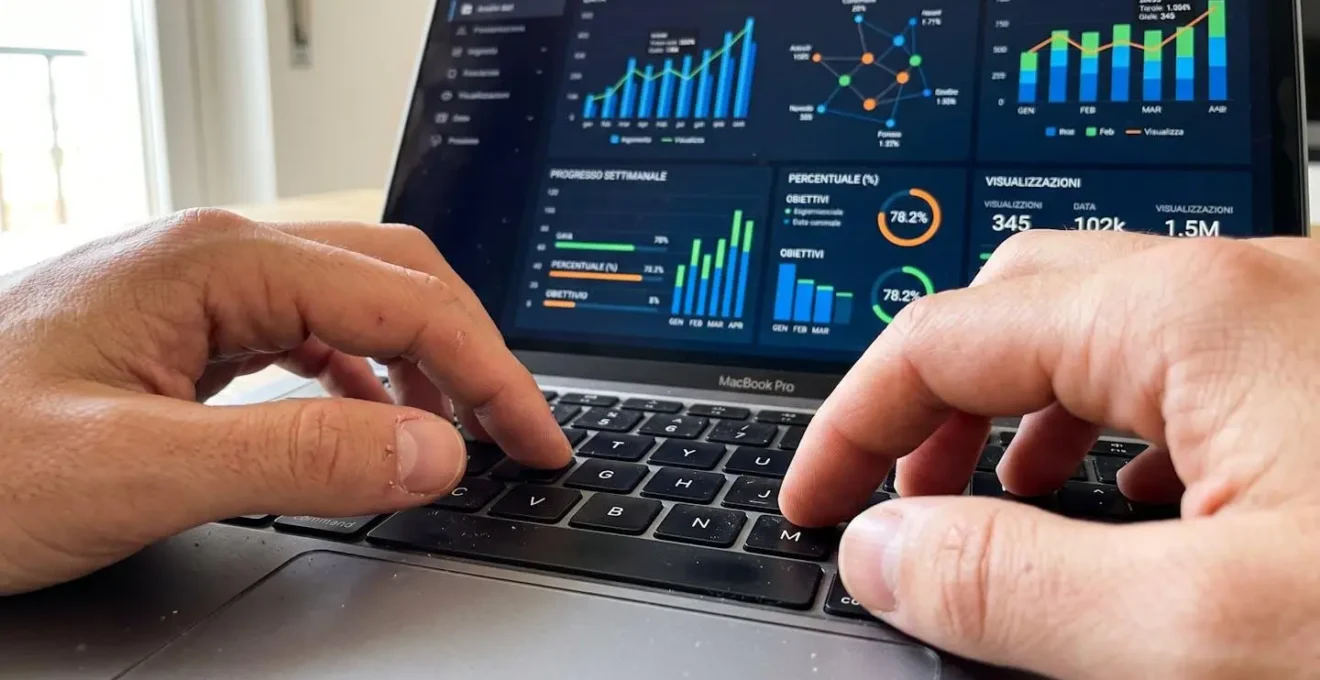 Primo piano ravvicinato di mani che digitano su tastiera di laptop moderno, schermo sullo sfondo completamente sfocato con grafici illeggibili, superficie scrivania contemporanea pulita